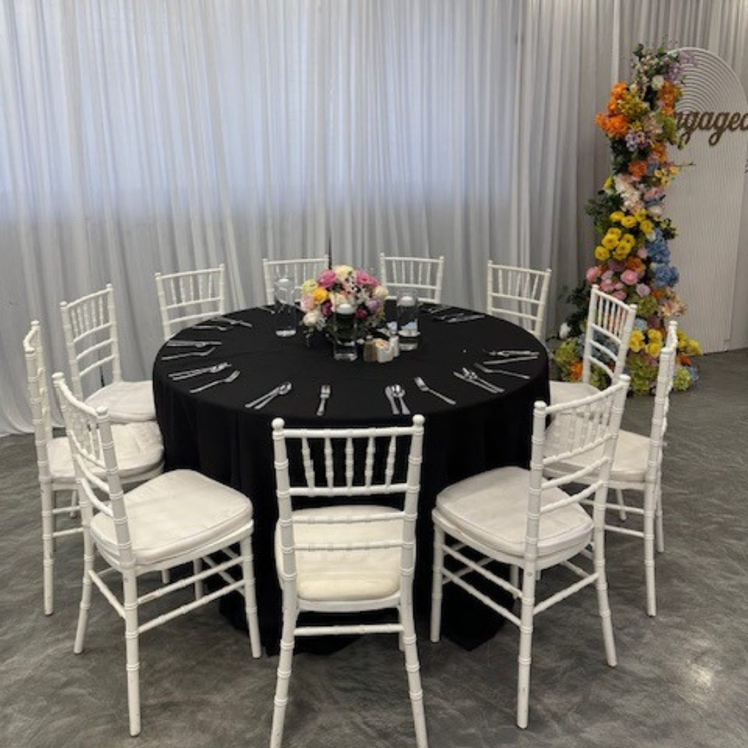 Round banquet table dressed in black with white chiavari chairs and florals